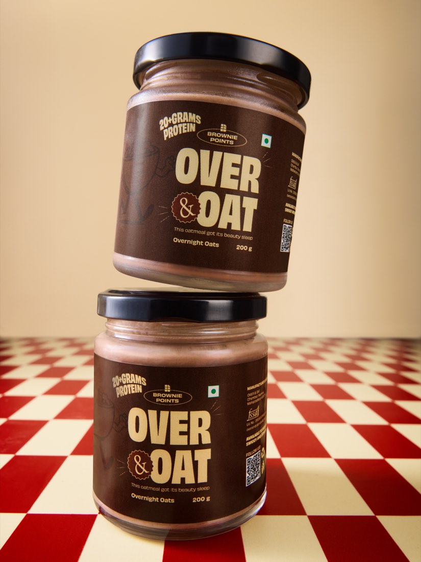 Two stacked jars of Over & Oat Brownie Points overnight oats on a red and cream checkerboard floor